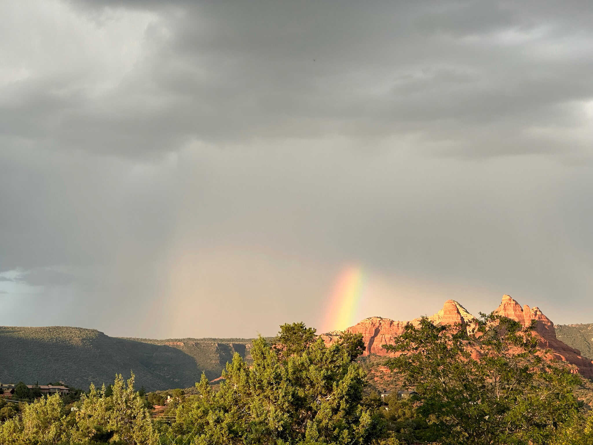A rainbow appears in the storm against the red rocks in Sedona