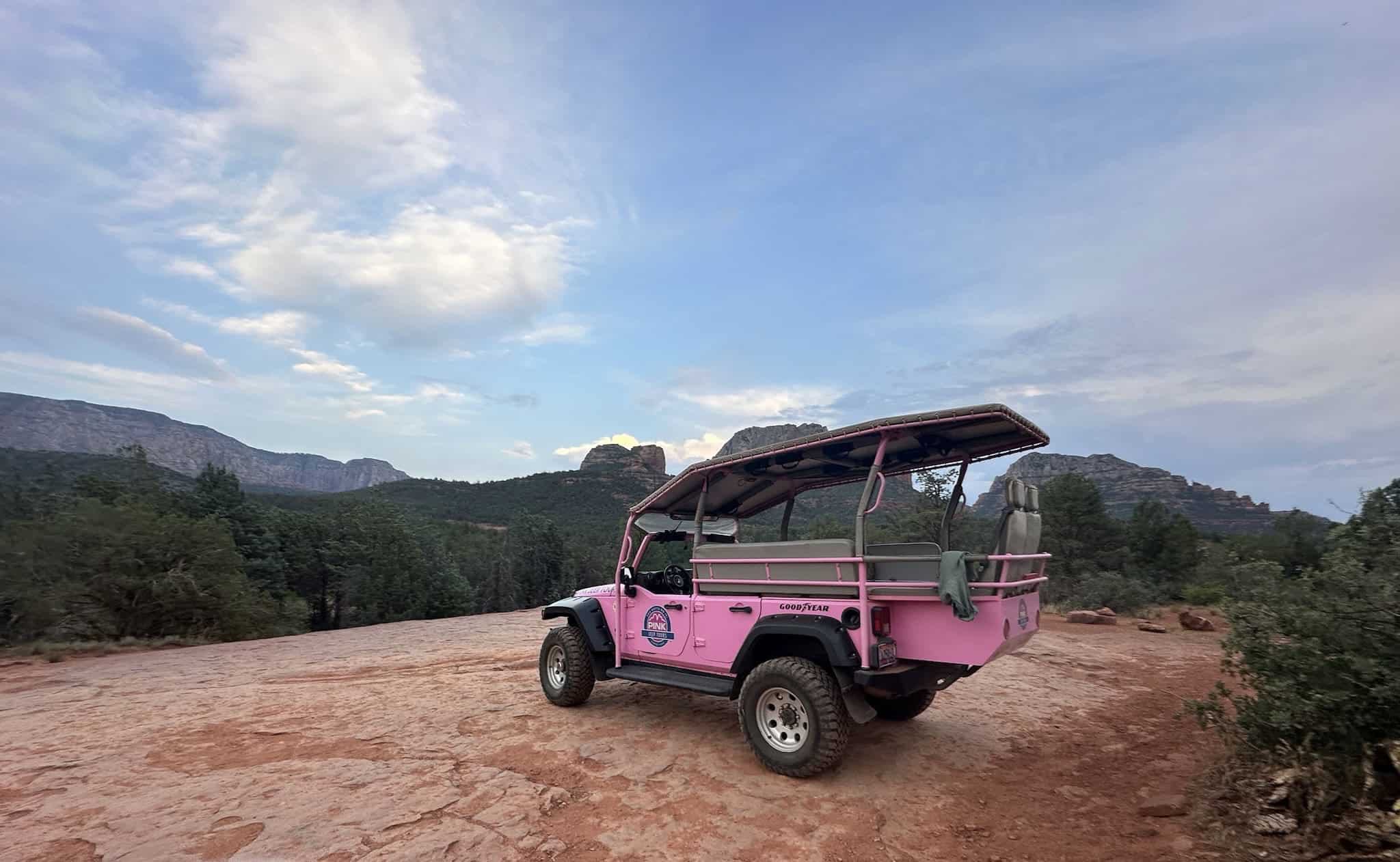A Pink Jeep on a ledge with Sedona's red rocks in the background.
