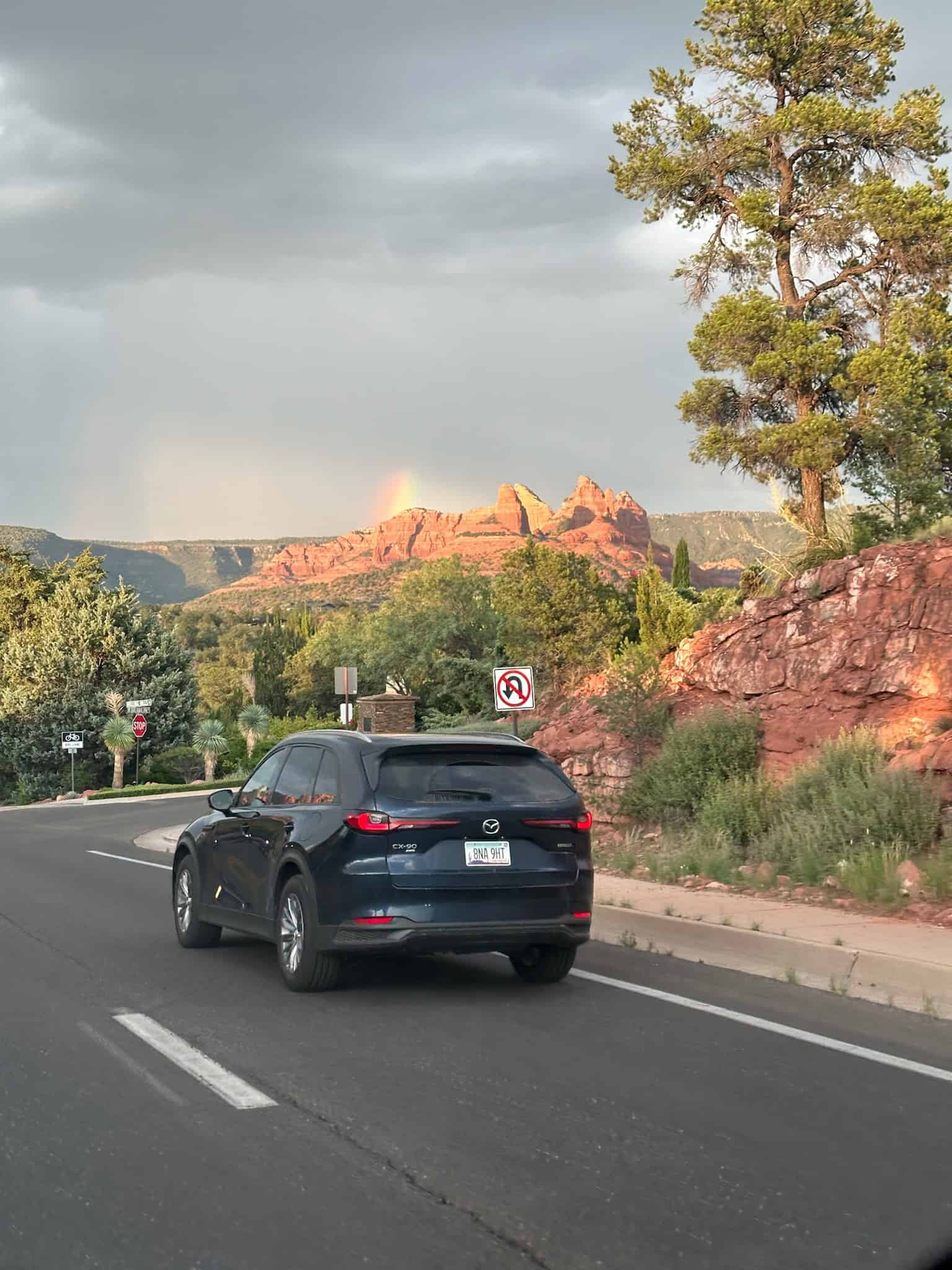 A vehicle driving in Sedona in monsoon season with a rainbow above the red rocks.