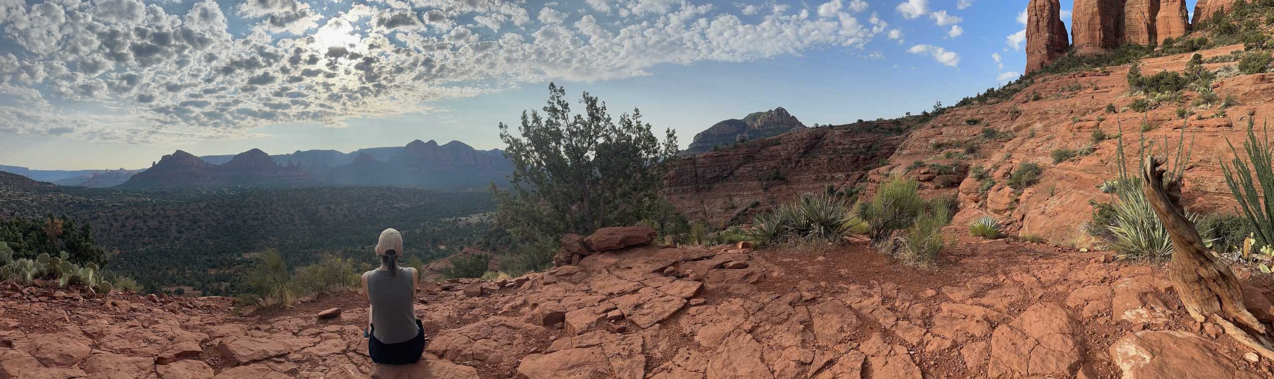 A woman sitting on a ledge looking at the Sedona's red rocks