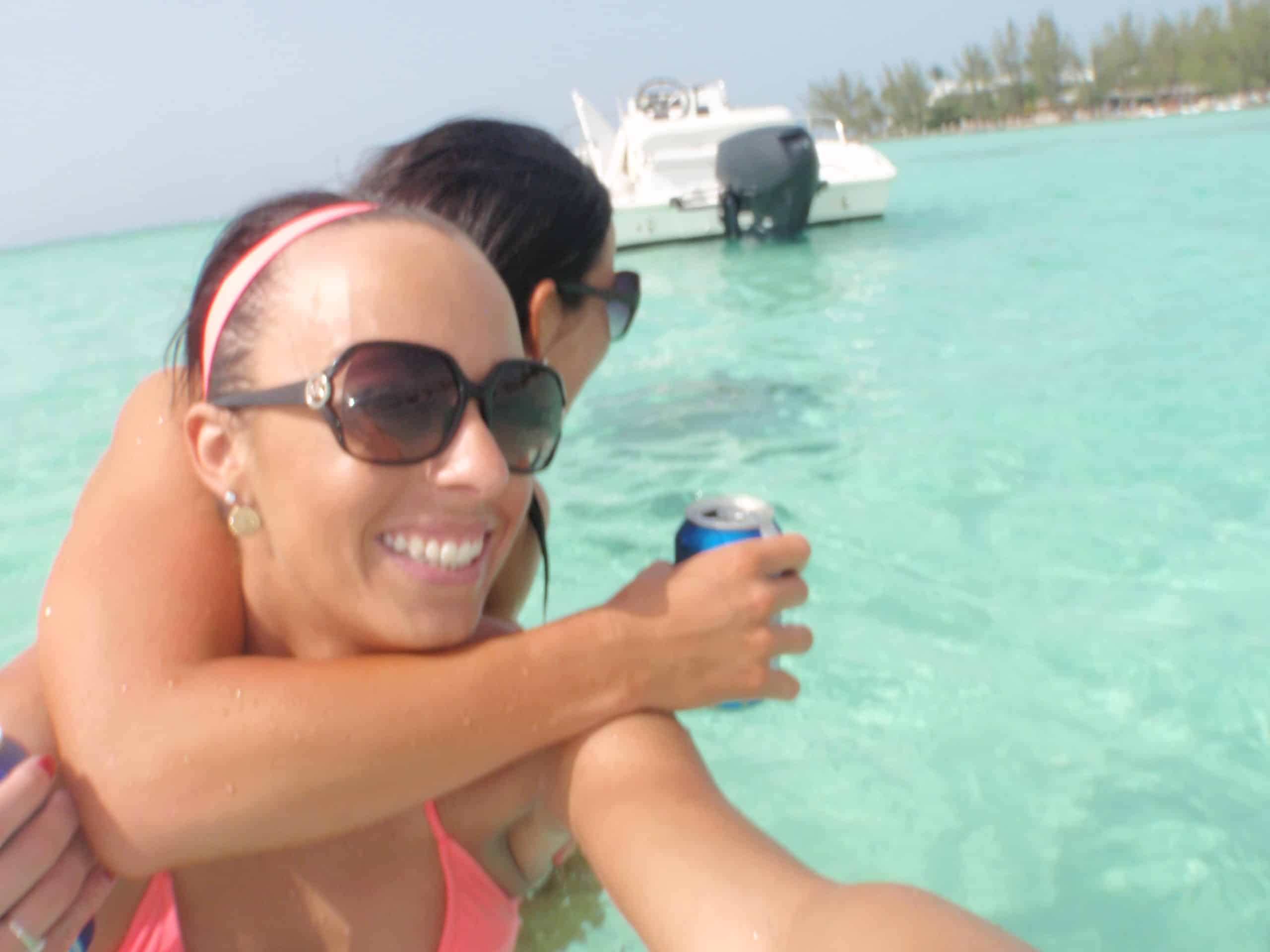 A girl hopping on another's back as a stingray approaches at Rum Point, Grand Cayman