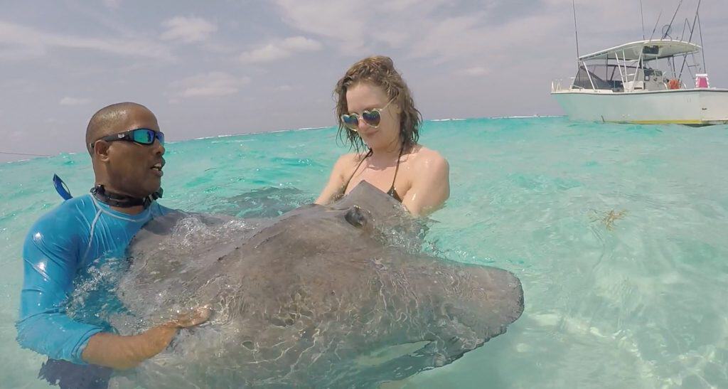 A woman holding a stingray with a tour guide at Grand Cayman's Stingray City