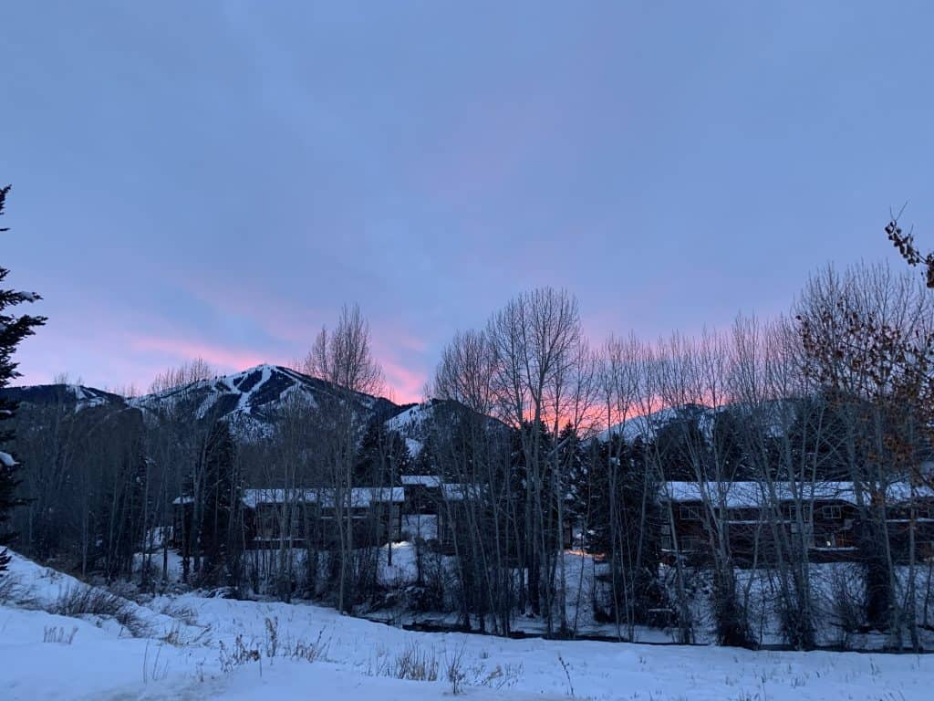 A view of a snowy mountain with pink sunset colors in the sky behind it